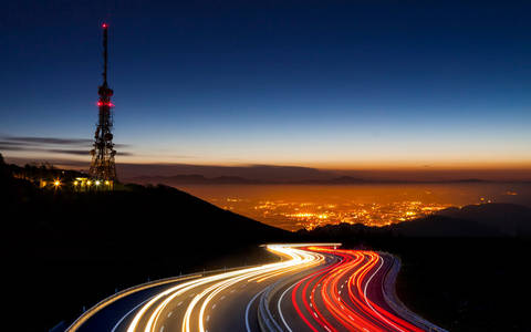 Car lights at night towards the city and communications antenna